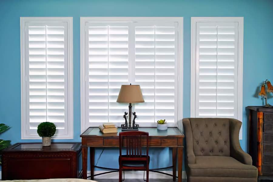 White Polywood shutters do double duty in beautifying your windows and insulating them. White Polywood shutters in a bedroom with bright blue walls